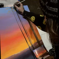 a woman painting a sunset on a canvas